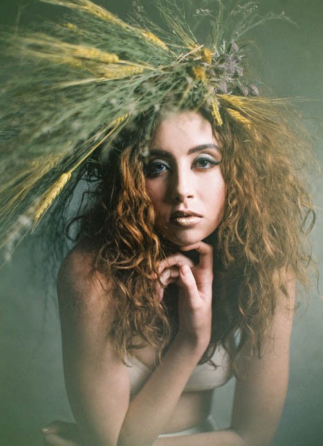 Young female model wearing dramatic headpiece with flowers and wheat.