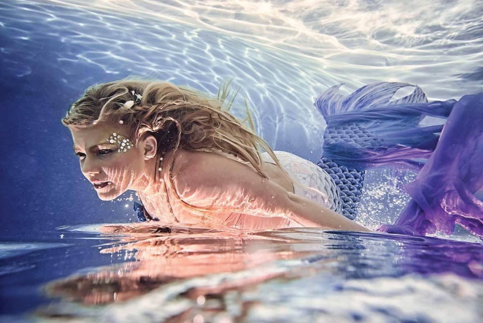 Blonde model wearing a purple mermaid costume underwater.
